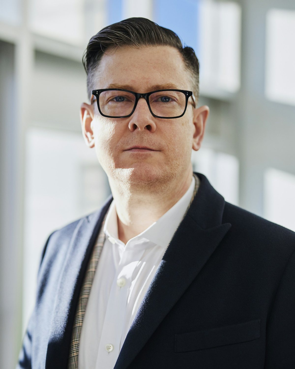 A confident business executive in a suit and glasses in a modern office.